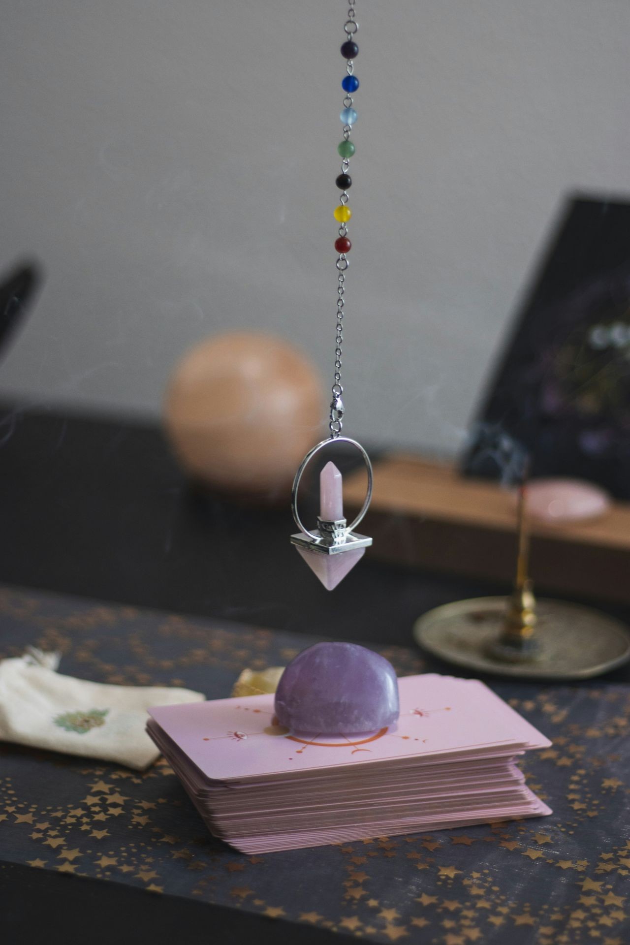 Pendulum with chakra beads and amethyst over tarot cards on a starry-patterned surface.